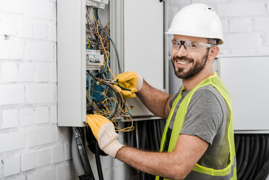 Smiling,Handsome,Electrician,Repairing,Electrical,Box,With,Pliers,In,Corridor